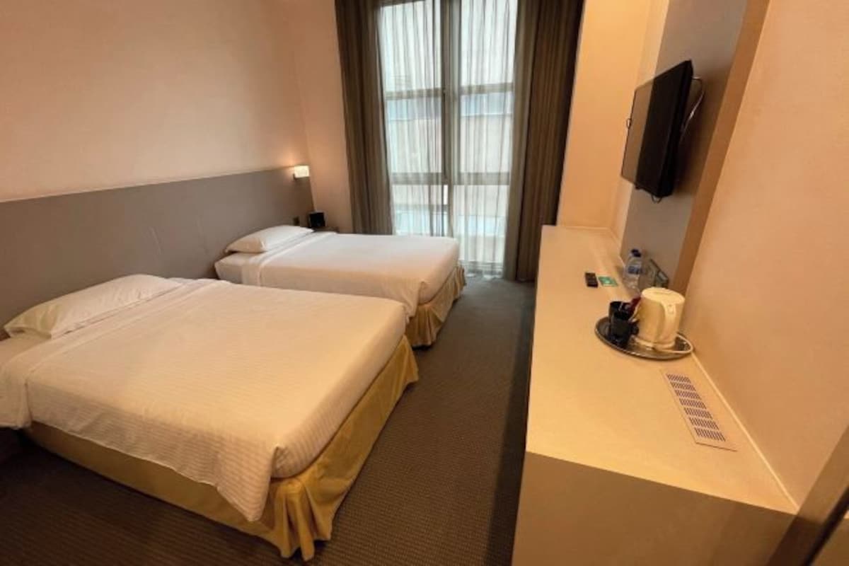 A hotel room with two beds, a bedside table with a cup and a tray, and a TV mounted on the wall.