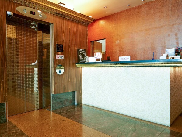 A reception area with a wooden wall, a glass elevator door, and a reception desk with a blue top. - Classique Hotel (Singapore)