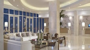 Un hall d’entrée spacieux avec un canapé blanc, des fauteuils, une table basse et un comptoir d’accueil.