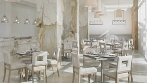 Un espace de salle à manger moderne avec des murs en marbre, des meubles blancs et des luminaires suspendus.