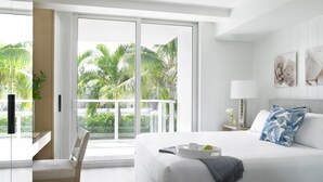 Une chambre d’hôtel moderne avec un grand lit, un bureau et une vue sur les palmiers, visible à travers les portes du balcon.