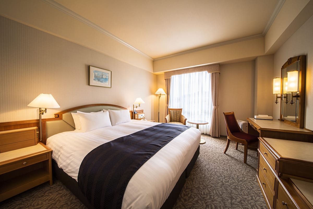 A hotel room with a large bed, a desk, a chair, and a dresser.