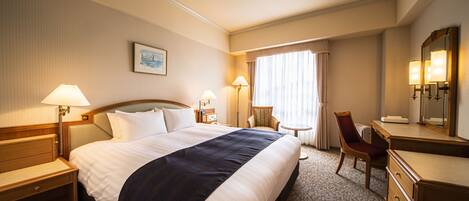 A hotel room with a large bed, a desk, a chair, and a dresser.