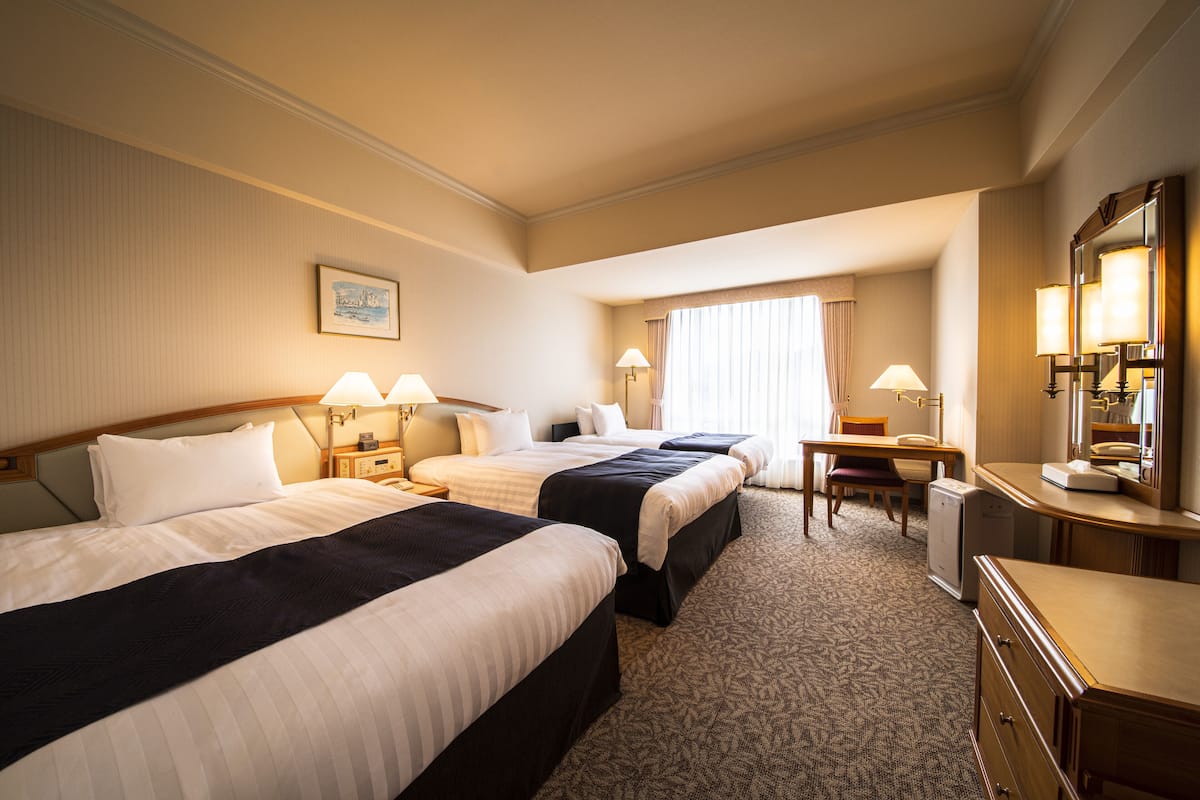 A hotel room with two beds, a desk, a chair, and a small refrigerator.