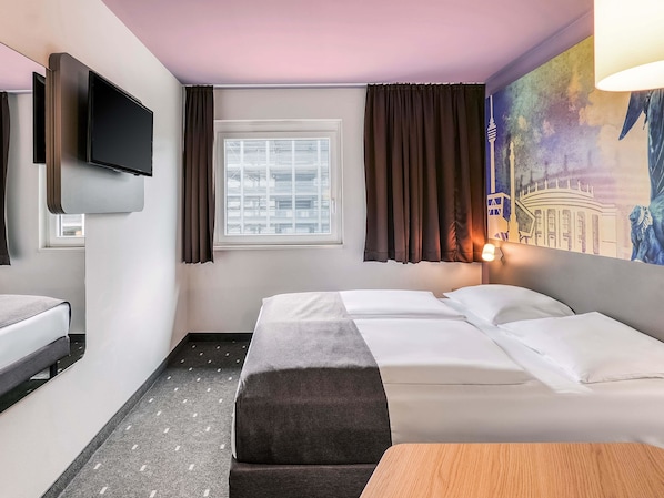 Una habitación de hotel con cama, escritorio, televisor, ventana con cortinas y un cuadro en la pared.