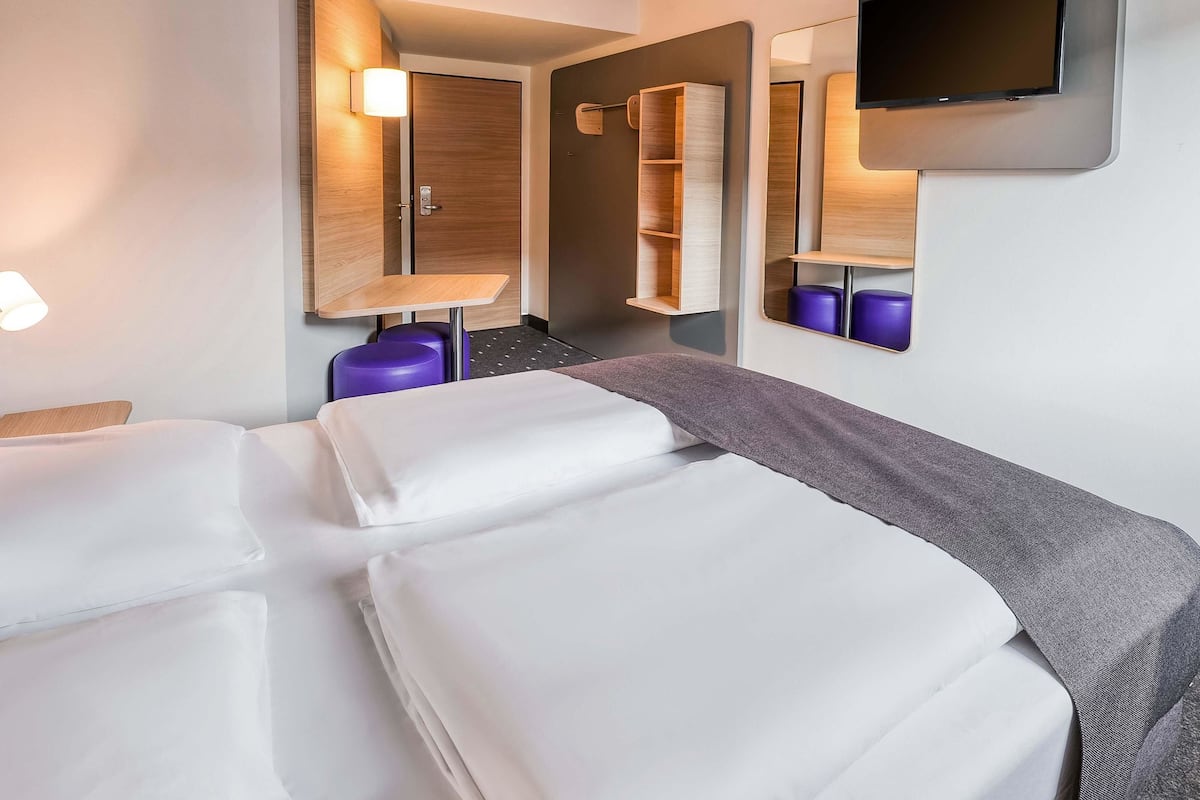 A hotel room with a bed, a desk, a chair, a mirror, and a TV.
