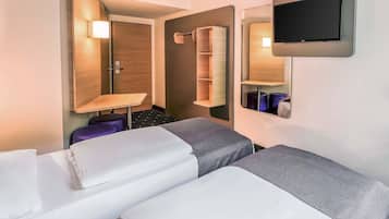 Ein Hotelzimmer mit zwei Betten, einem an der Wand montierten Fernseher, einem Holzschrank und einem kleinen Tisch mit einer Lampe.