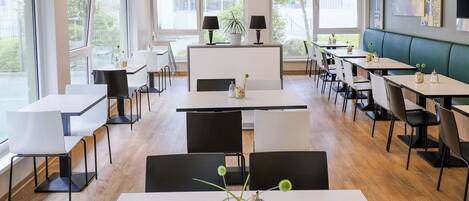 Un espace de restauration moderne, doté de plusieurs tables et chaises, de grandes fenêtres laissant entrer la lumière naturelle et offrant une vue sur l’extérieur.