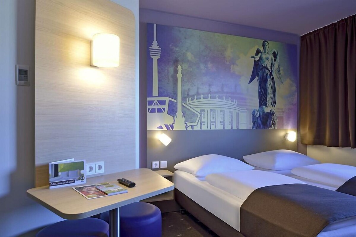 Habitación de hotel con cama, escritorio y lámpara fijada a la pared.