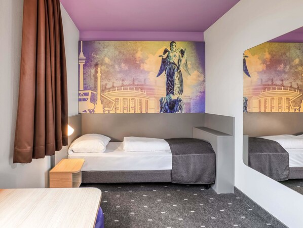 A hotel room with a bed, a small wooden table, a mirror, and a wall with a mural. - B&B Hotel Stuttgart-Vaihingen (Stuttgart)