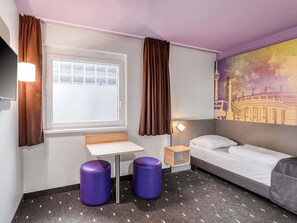 A hotel room with a bed, a small table, two purple stools, a window with curtains, and a wall mural. - B&B Hotel Stuttgart-Vaihingen (Stuttgart)