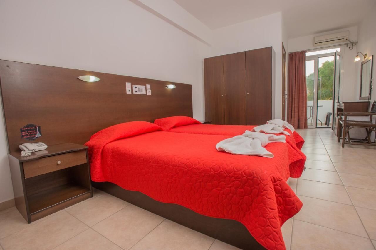 Habitación de hotel con una cama grande, cabecera de madera, mesita de noche con un teléfono y vistas al exterior a través de una puerta de vidrio.