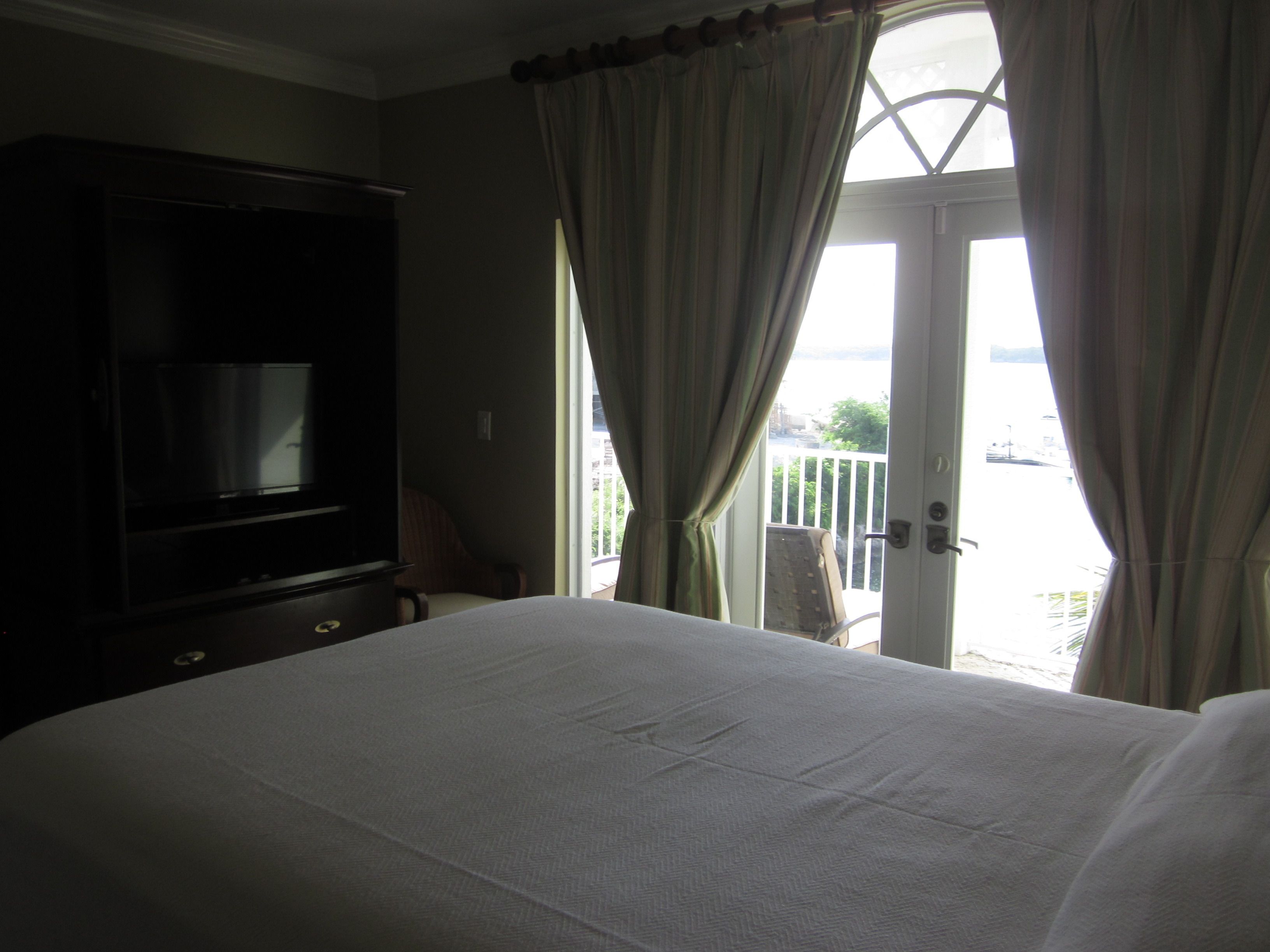 Une chambre d’hôtel avec un lit, une télévision et un balcon avec des rideaux.