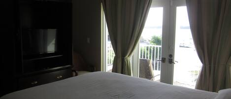 Une chambre d’hôtel avec un lit, une télévision et un balcon avec des rideaux.