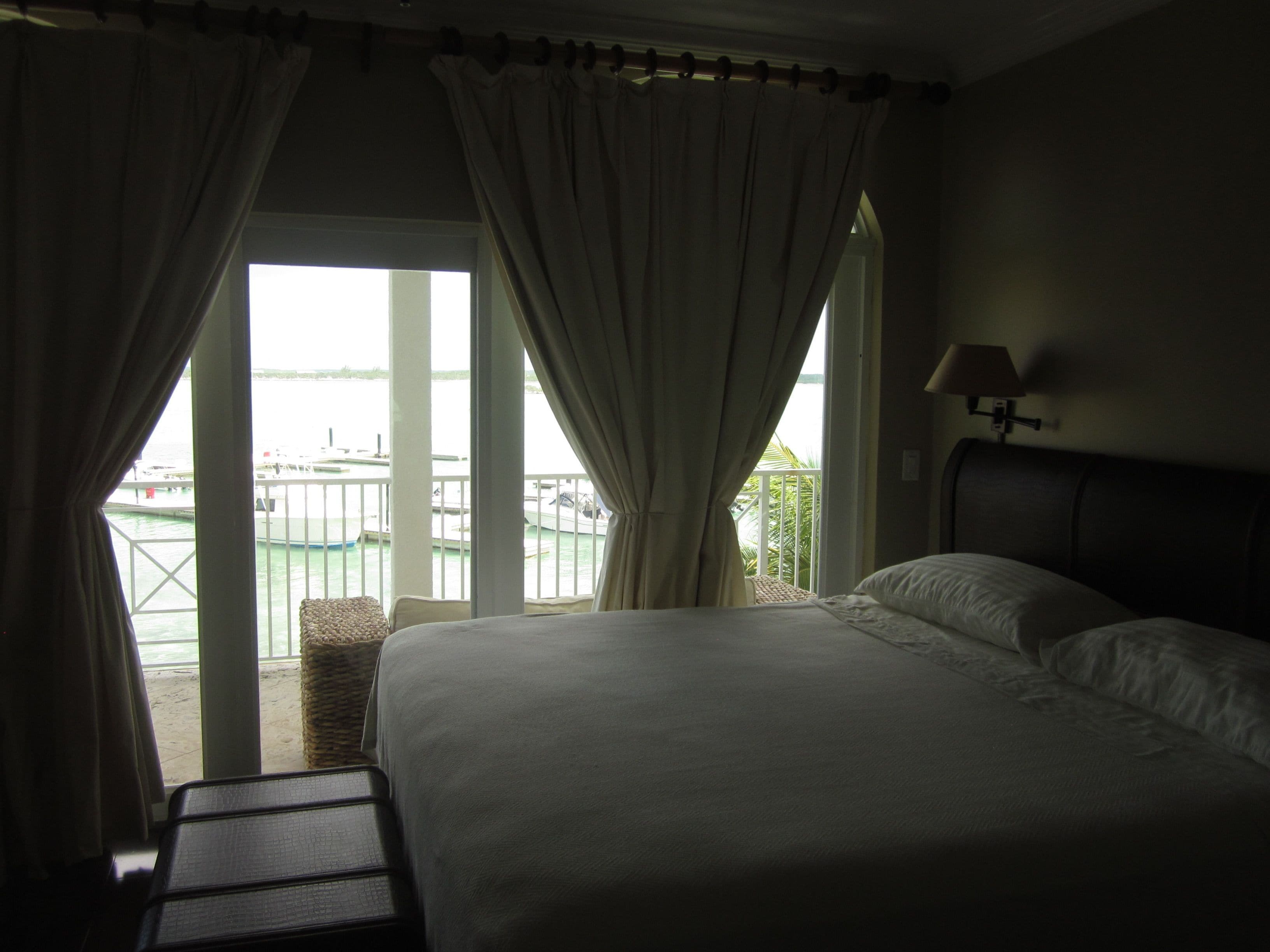 Ein Hotelzimmer mit Bett, kleinem Tisch und Vorhängen. Durch das Fenster ist Wasser und ein Boot zu sehen.