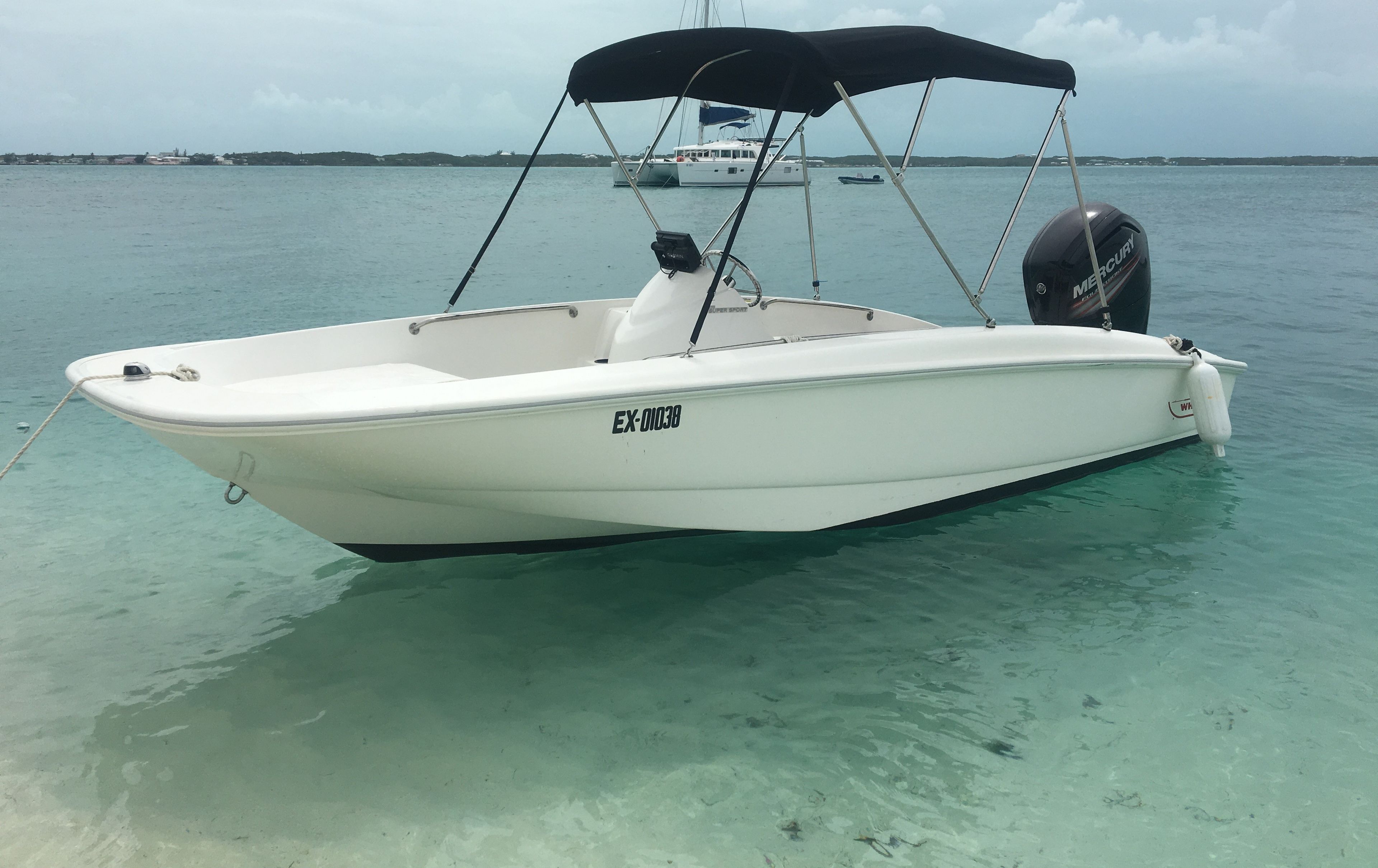 A white boat with a black canopy, labeled EX-01038, docked in clear turquoise water.
