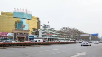 Una calle con edificios, incluyendo una gran estructura amarilla con un cartel, un edificio blanco con varias ventanas, y un cartel azul.