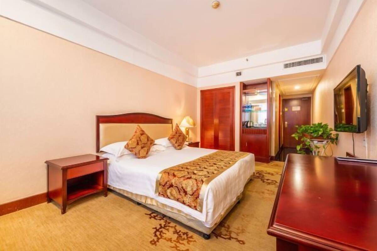 Ein Hotelzimmer mit einem Bett, einem Nachttisch, einer Kommode und einem an der Wand befestigten Fernseher.