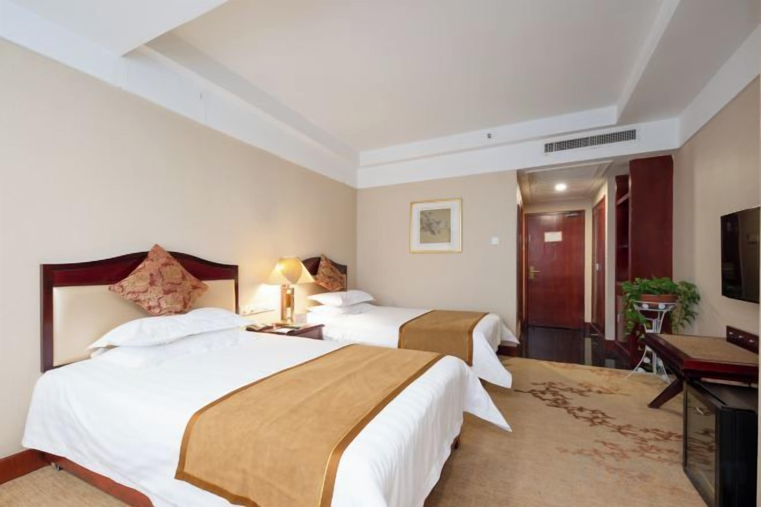 Habitación de hotel con dos camas, televisión, escritorio y puerta que da a otra habitación.