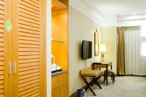 Habitación de hotel con un armario de madera, un escritorio con una silla, un televisor y una ventana con cortinas.
