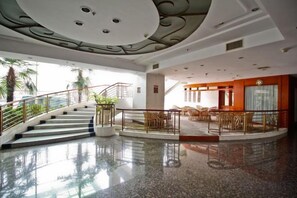 Een hotelhal met een centrale trap, een zithoek en een receptiebalie.