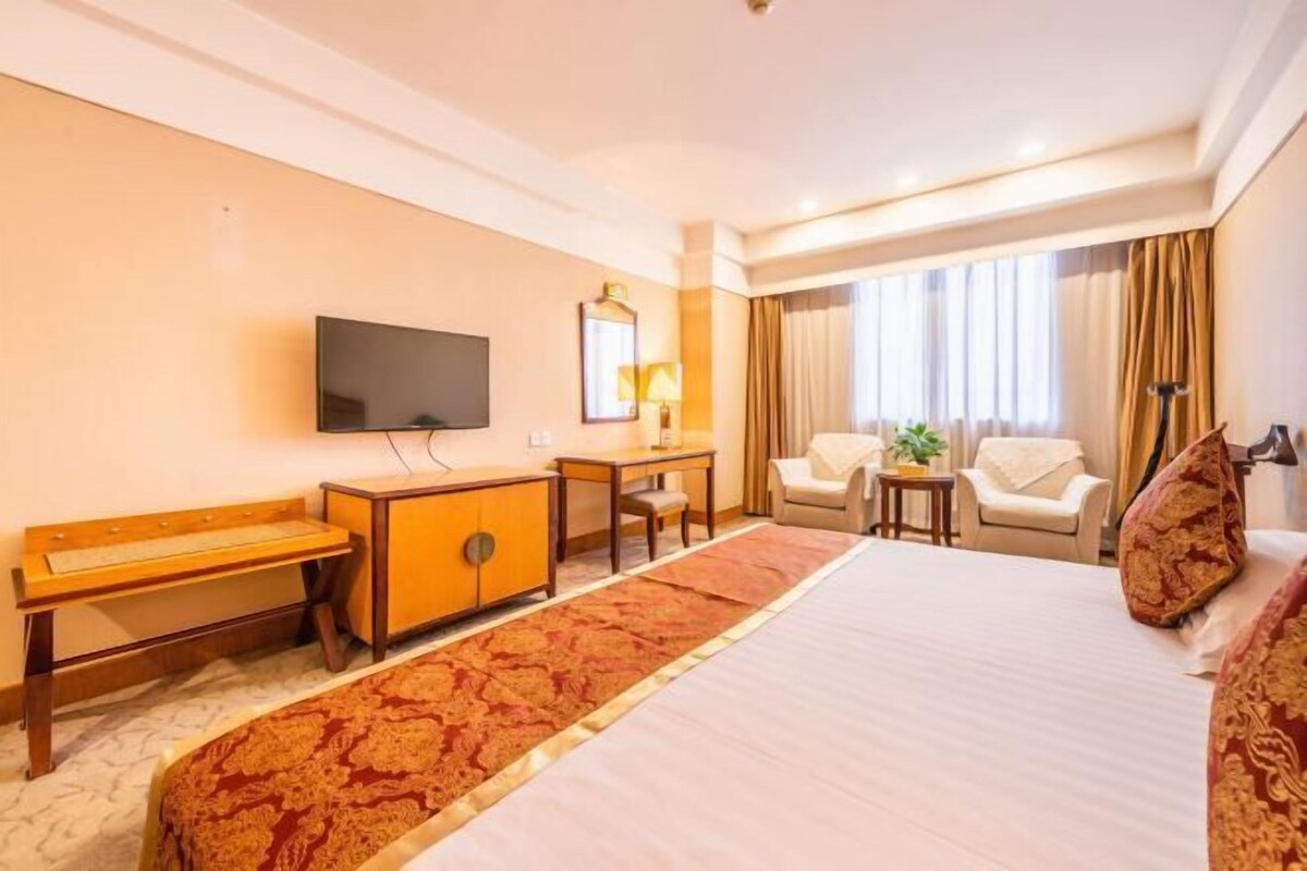 A hotel room with a bed, a TV, a desk, a chair, and a small table.