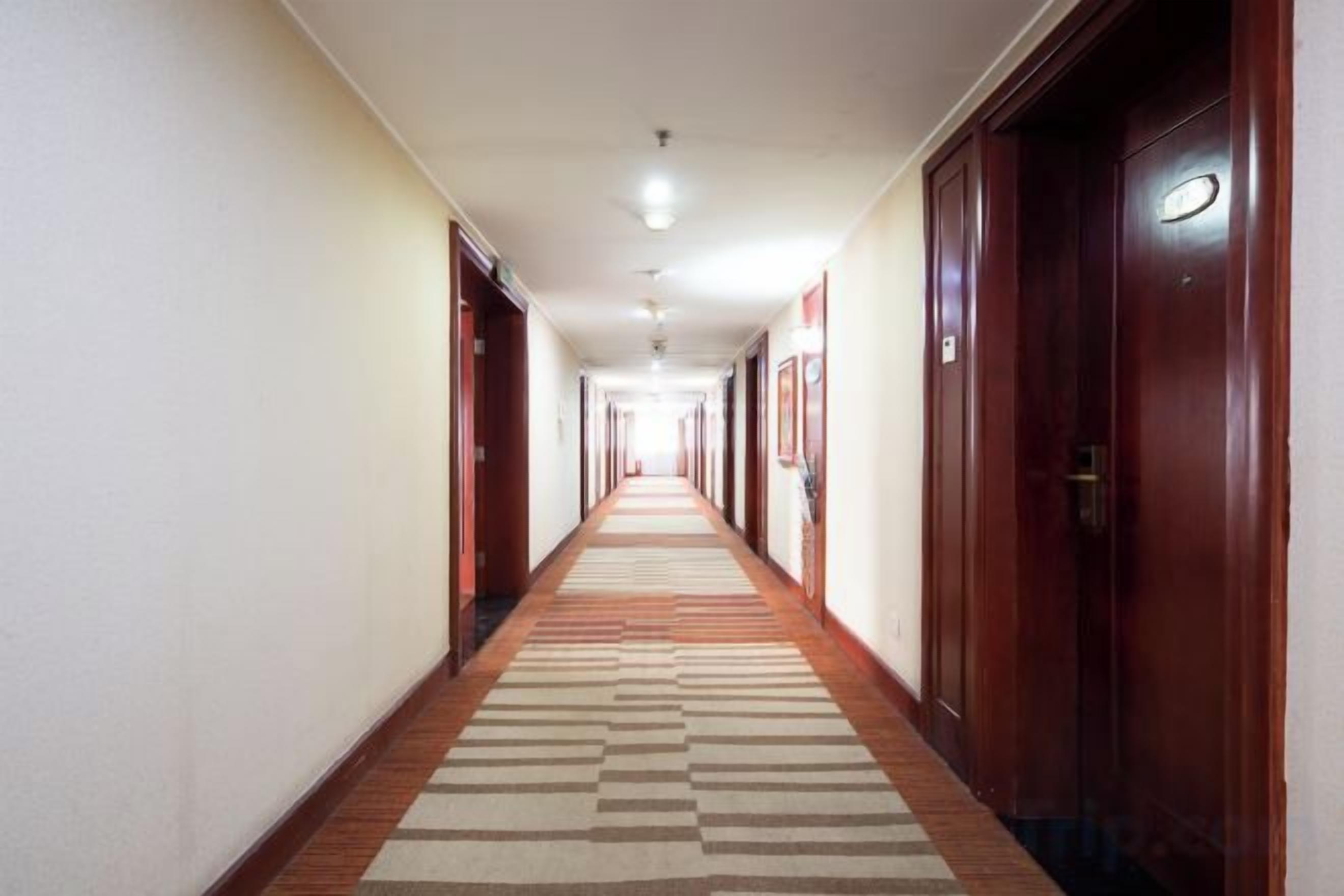 Pasillo de hotel con puertas a ambos lados, alfombra estampada e iluminación empotrada en el techo.