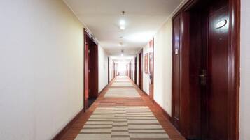 Pasillo de hotel con puertas a ambos lados, alfombra estampada e iluminación empotrada en el techo.