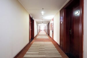 Pasillo de hotel con puertas a ambos lados, alfombra estampada e iluminación empotrada en el techo.