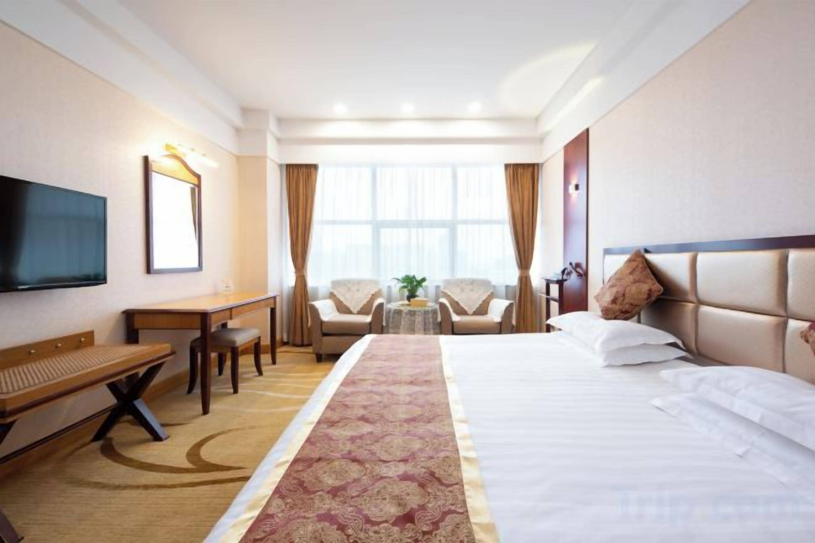 Ein Hotelzimmer mit Bett, Schreibtisch, Stuhl, Fernseher und einem Fenster mit Vorhängen.