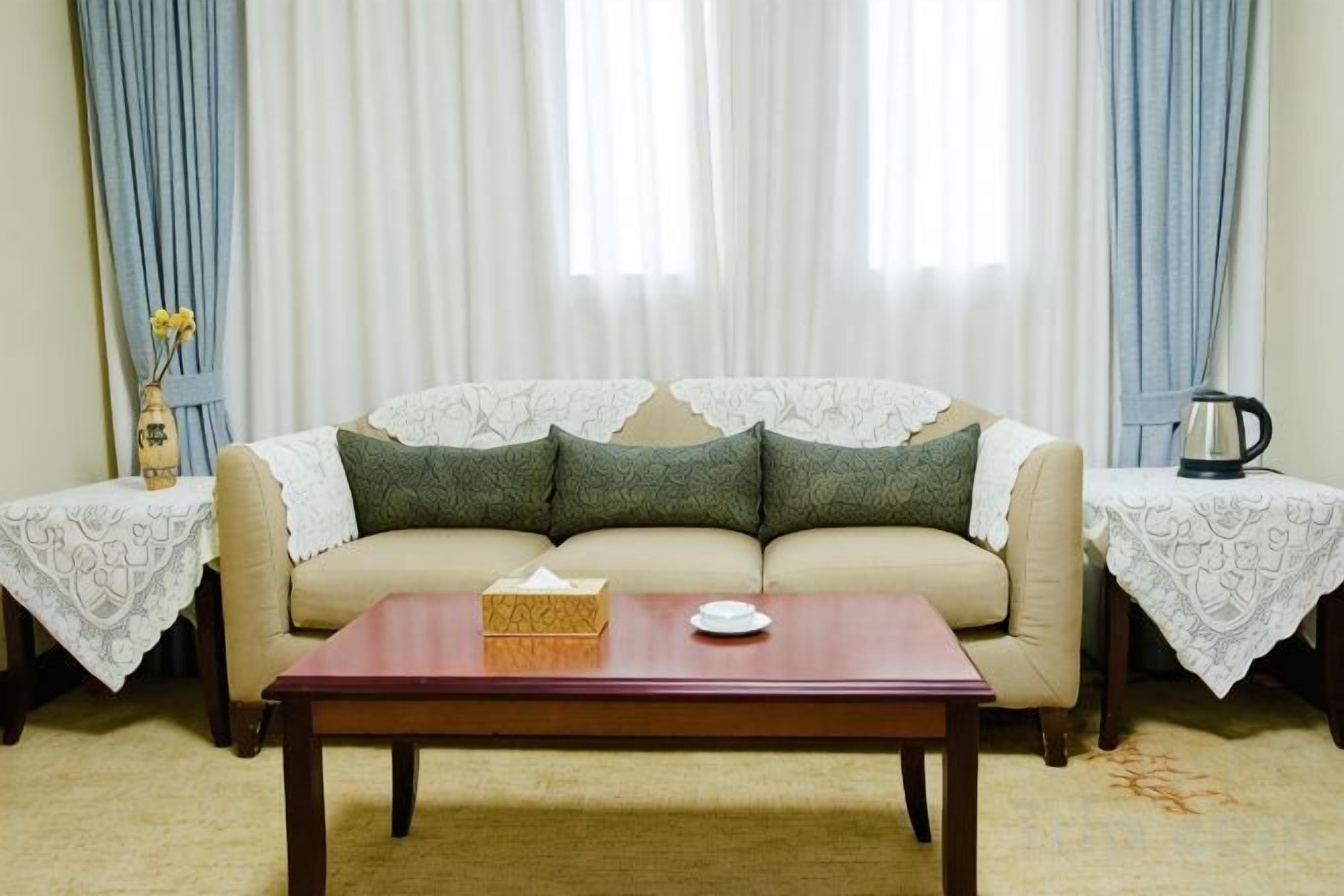 Un salon avec un canapé, une table basse, un vase de fleurs et une bouilloire posée sur une table d’appoint.