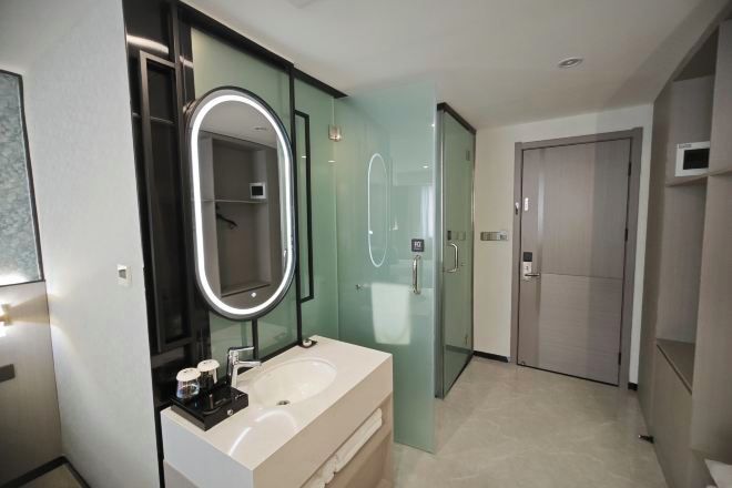 A modern bathroom with a glass-enclosed shower, a large mirror with a light, and a white sink.
