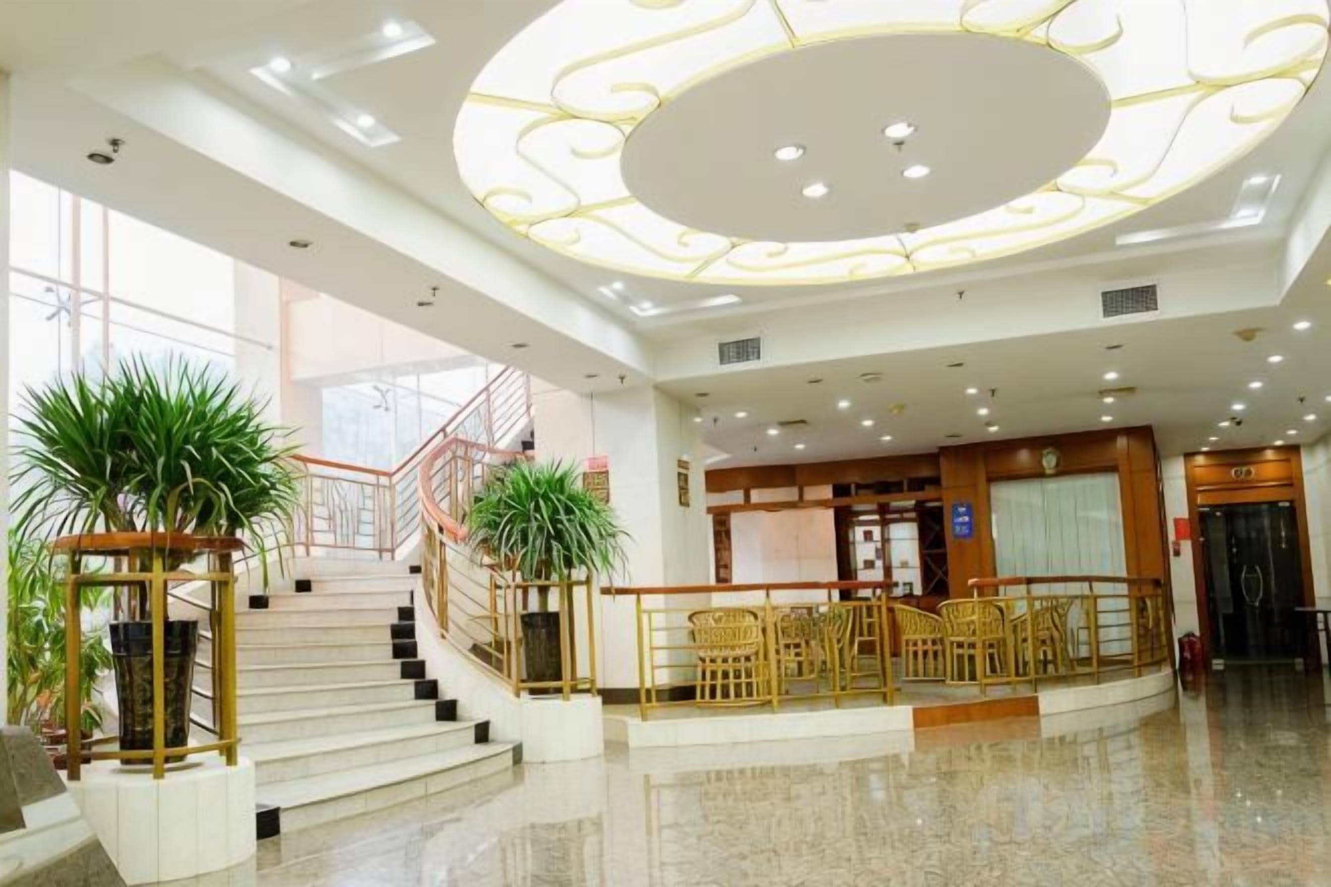 A hotel lobby with a grand staircase, a reception desk, and a seating area.
