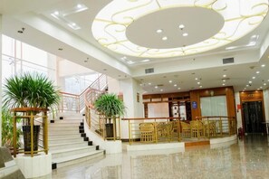 A hotel lobby with a grand staircase, a reception desk, and a seating area.