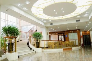 Un vestíbulo de hotel con una imponente escalera, una recepción y un área de descanso.