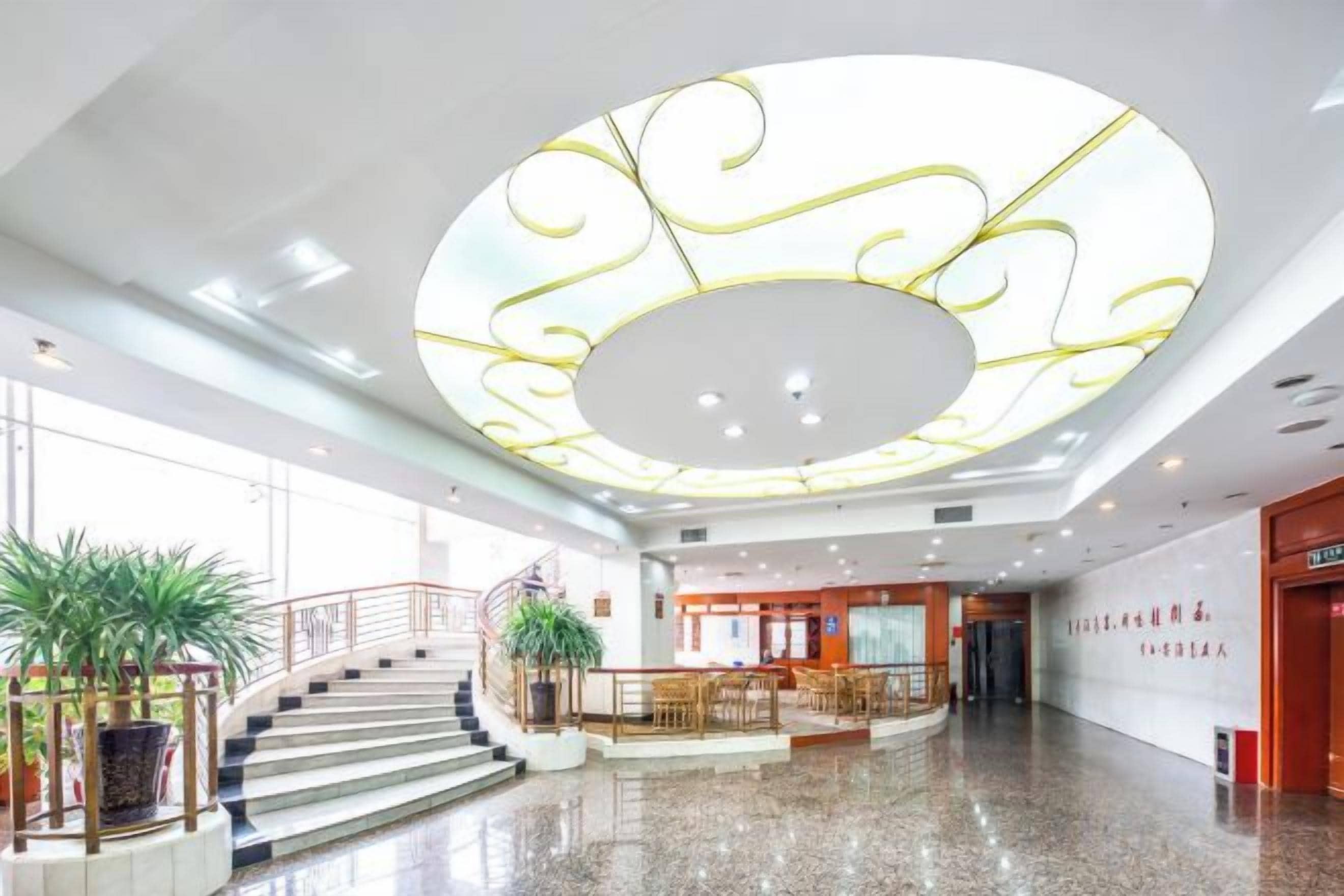 Eine großzügige Lobby mit einer zentralen Treppe, einem Empfangsbereich und einem großen, runden Deckenmuster.