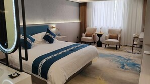Ein Hotelzimmer mit einem großen Bett, zwei Sesseln, einem kleinen Tisch und einem großen Fenster mit Vorhängen.