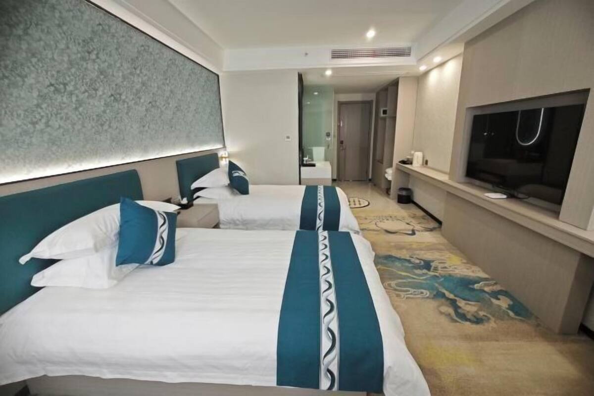 Ein Hotelzimmer mit zwei Betten, einem Fernseher und einem sichtbaren Badezimmer im Hintergrund.