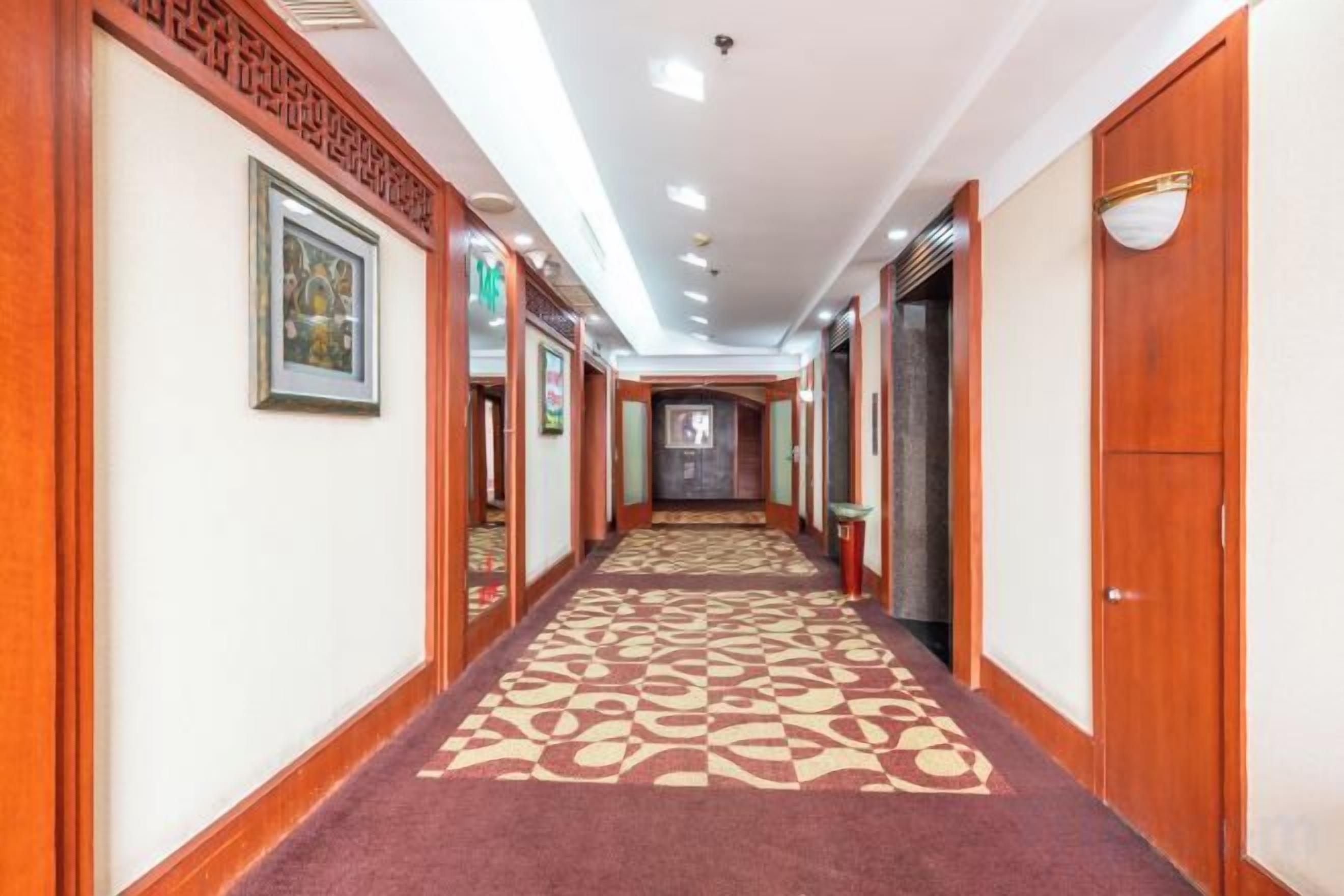 A hotel corridor with a patterned carpet, wooden doors, and framed artwork on the walls.