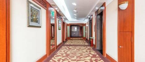 A hotel corridor with a patterned carpet, wooden doors, and framed artwork on the walls.