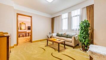 Habitación de hotel con sofá, una mesita de centro, una planta y vistas al exterior a través de amplias ventanas.