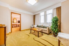 A hotel room with a sofa, a coffee table, a plant, and a view of the outside through large windows. - Jinmao International Hotel (HUAINAN)