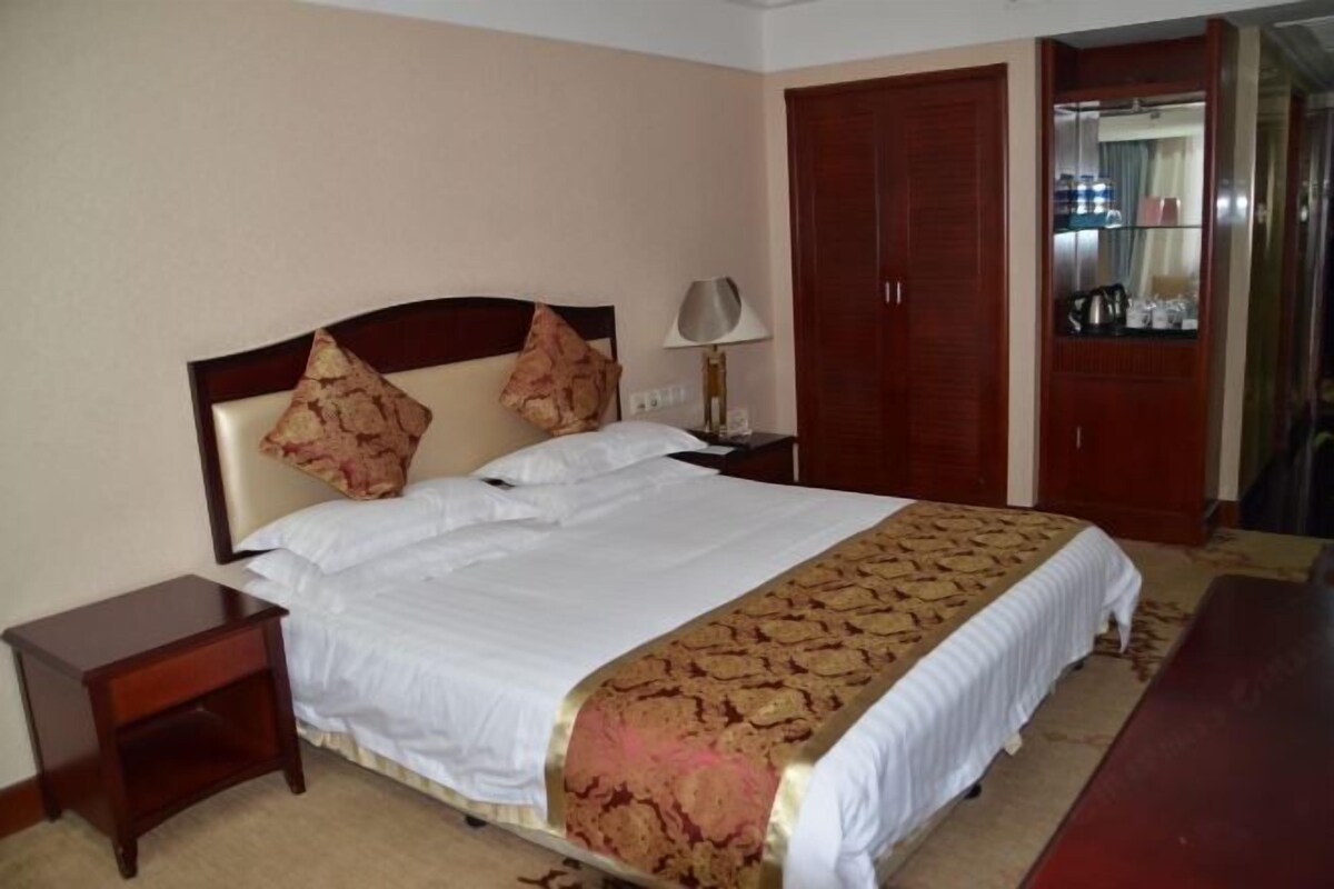 A hotel room with a bed, a nightstand, a lamp, a wardrobe, and a mirror.