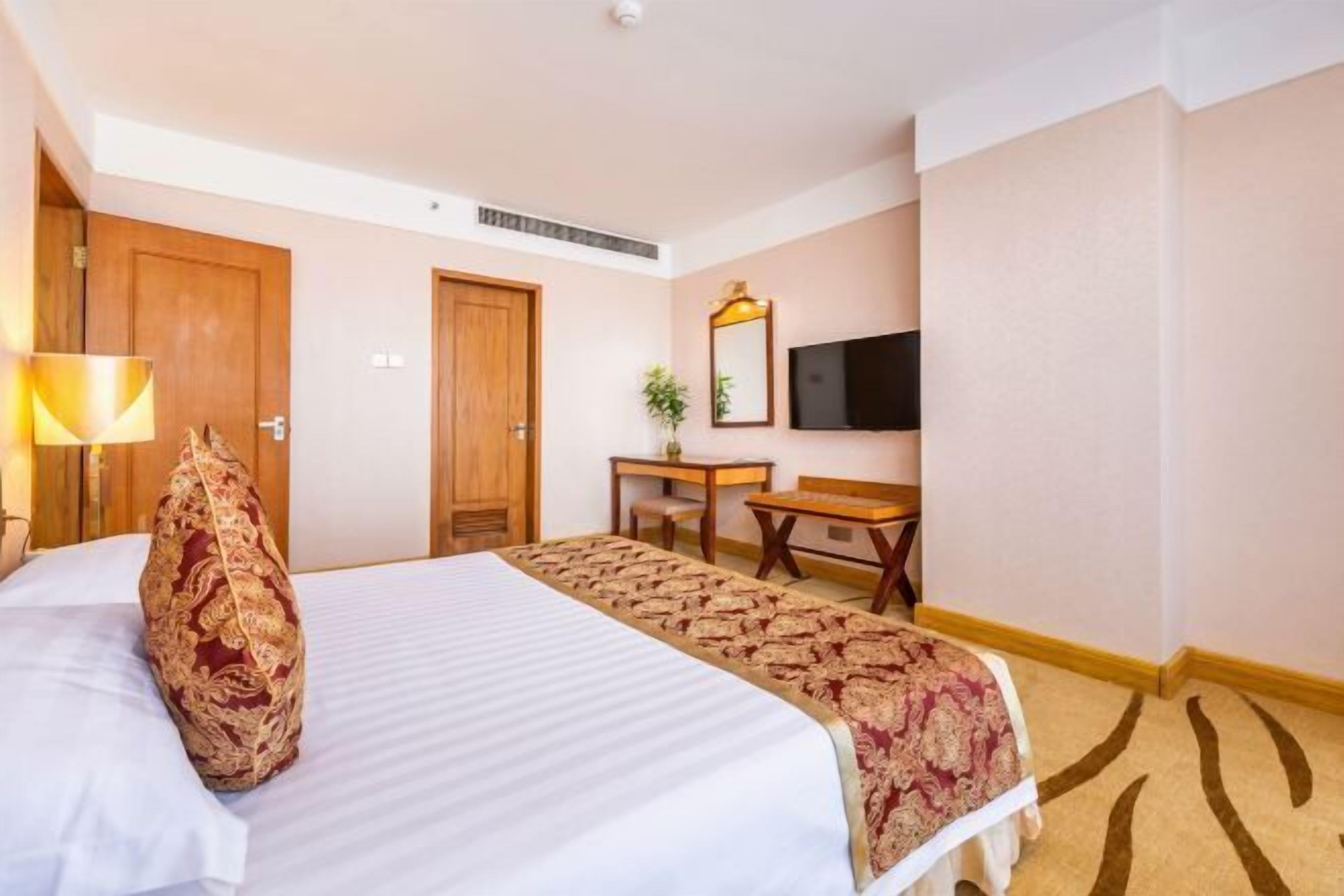 Habitación de hotel con cama, escritorio, silla, televisor y espejo.