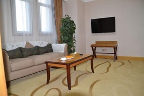 Ein Wohnzimmer mit einer Couch, einem Couchtisch, einer Pflanze und einem Fernseher an der Wand.
