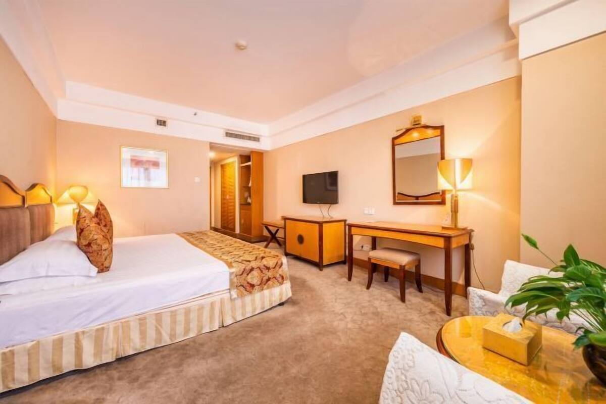 Ein Hotelzimmer mit zwei Betten, einem Schreibtisch, einem Sessel, einem Fernseher, einem Spiegel und einer Pflanze.