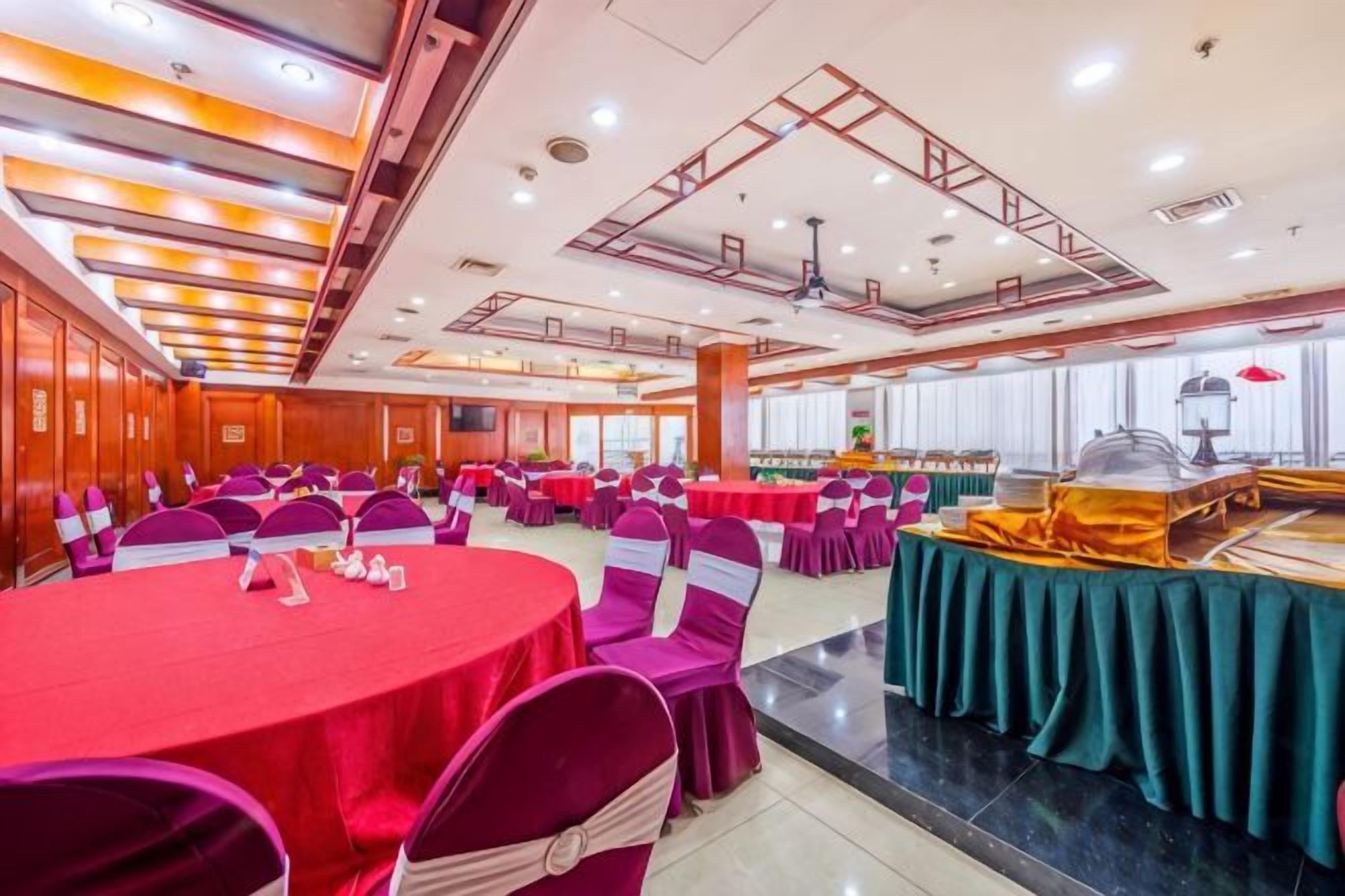 Un salón de banquetes con mesas redondas, sillas y una barra de buffet.