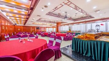 Un salón de banquetes con mesas redondas, sillas y una barra de buffet.
