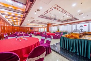 Une salle de banquet avec des tables rondes, des chaises et un buffet.