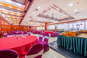 Un salón de banquetes con mesas redondas, sillas y una barra de buffet.
